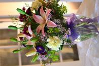 Sweet Garden. A clear ginger jar glass vase with purple motsimoto daisies, sweet yellow roma carnations, pink lilies, purple mums and lavender wax flower. Adorned with a purple bow.