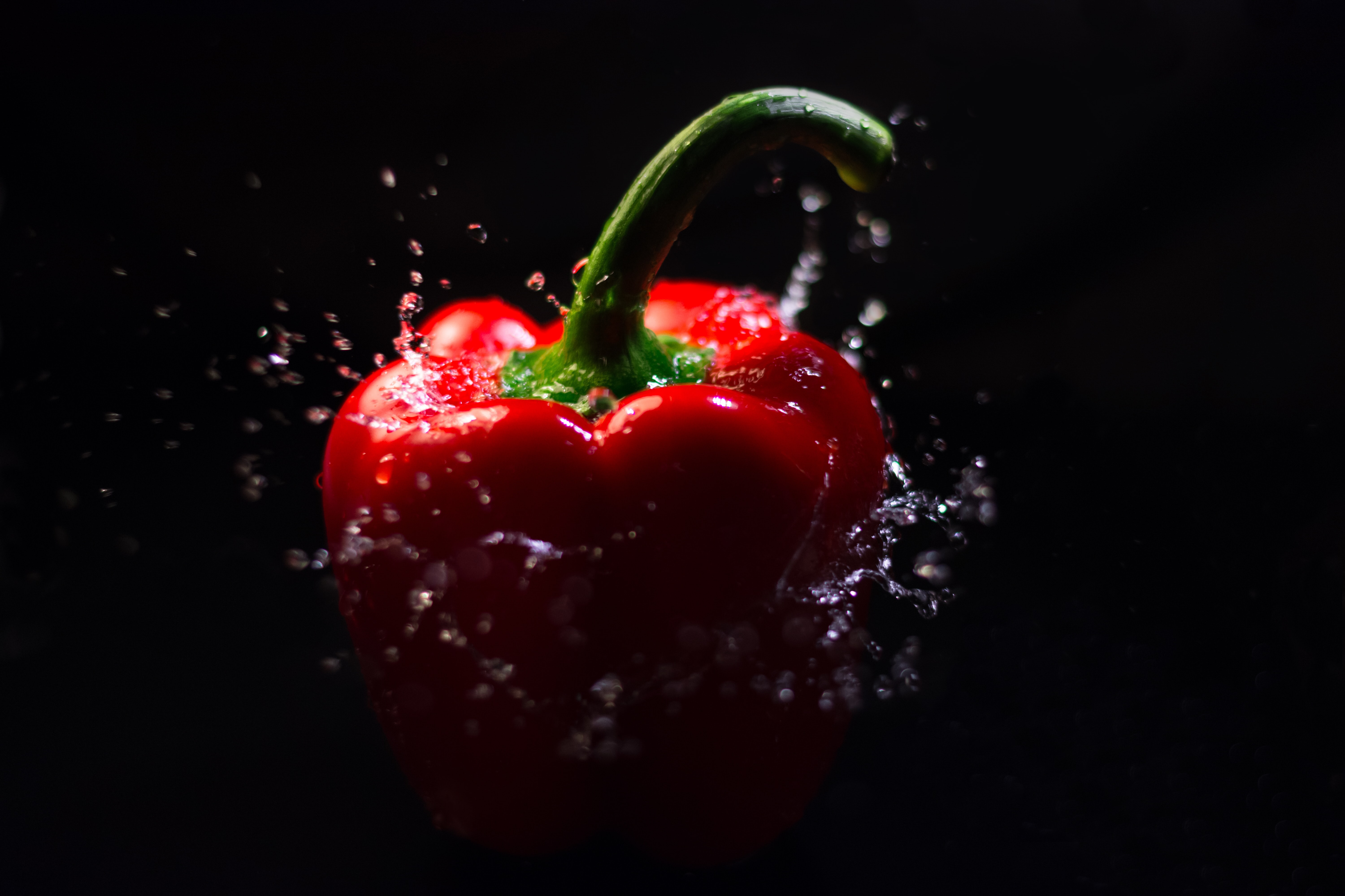 A red bell pepper splashing into water in front of a dark black background.