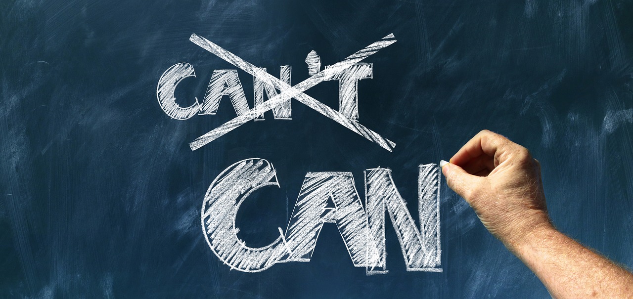 A person crosses out the word “Can’t” while leaving the word can on a chalkboard.