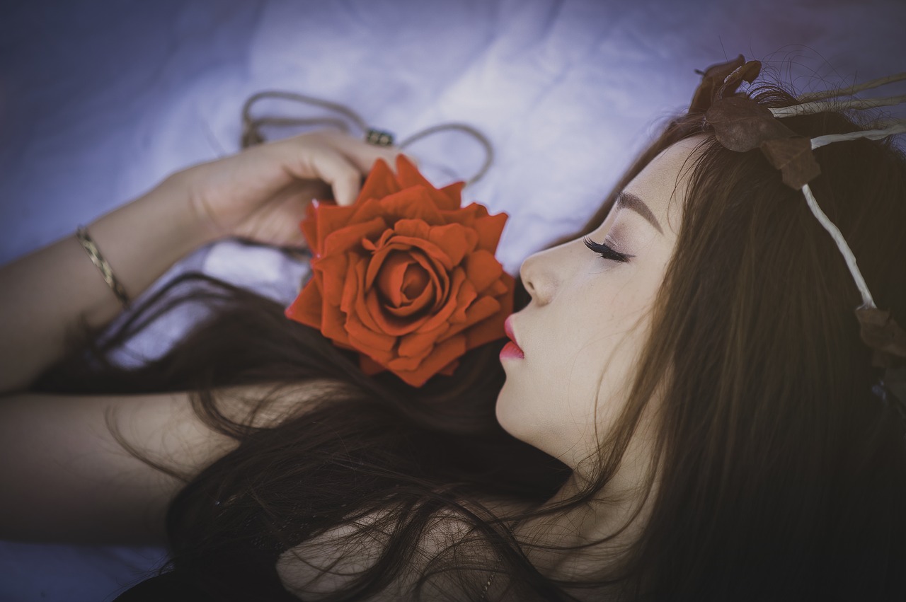 A woman sleeps comfortably on a bed while holding a rose.
