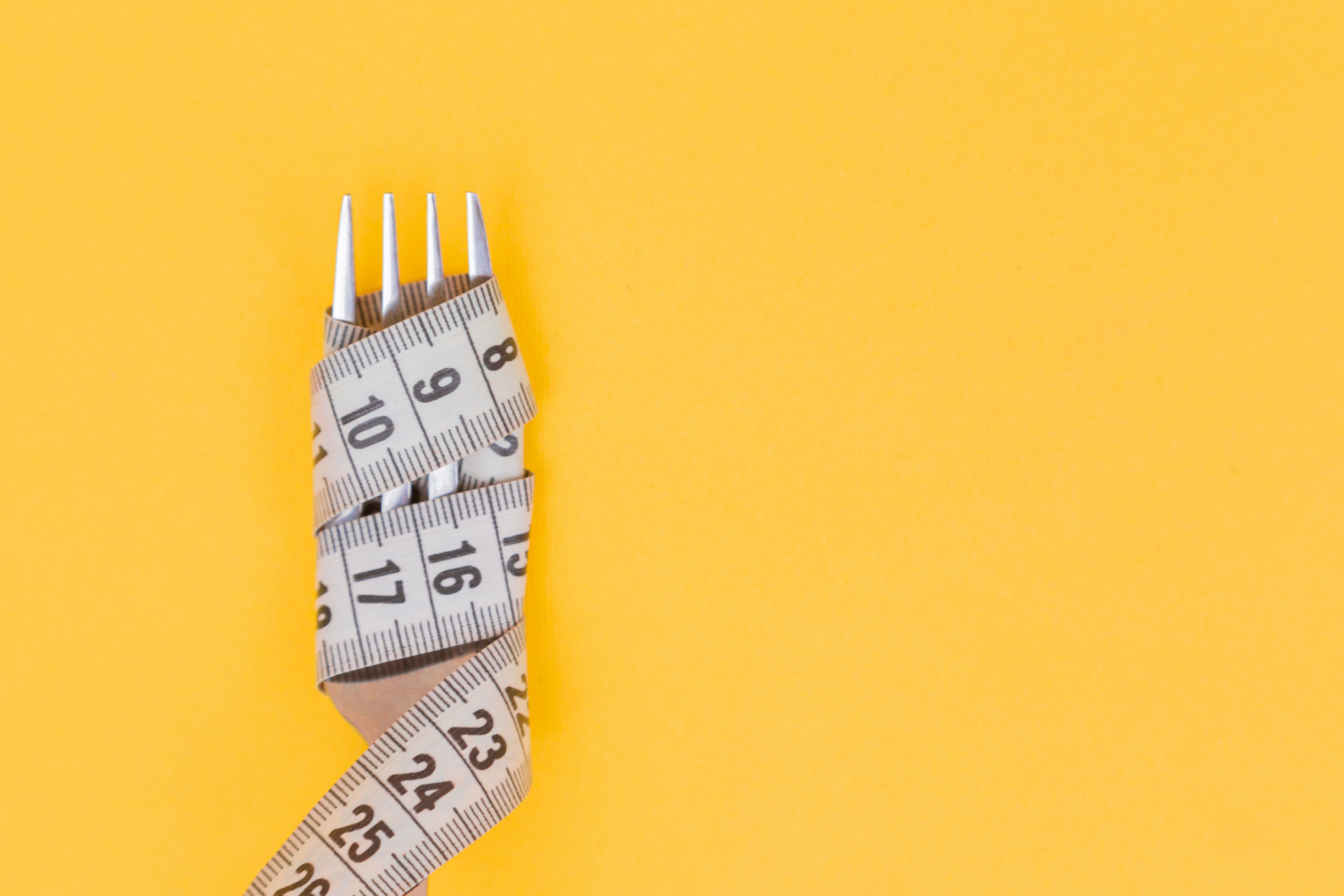 A tape measure wrapped around a fork with a yellow background.