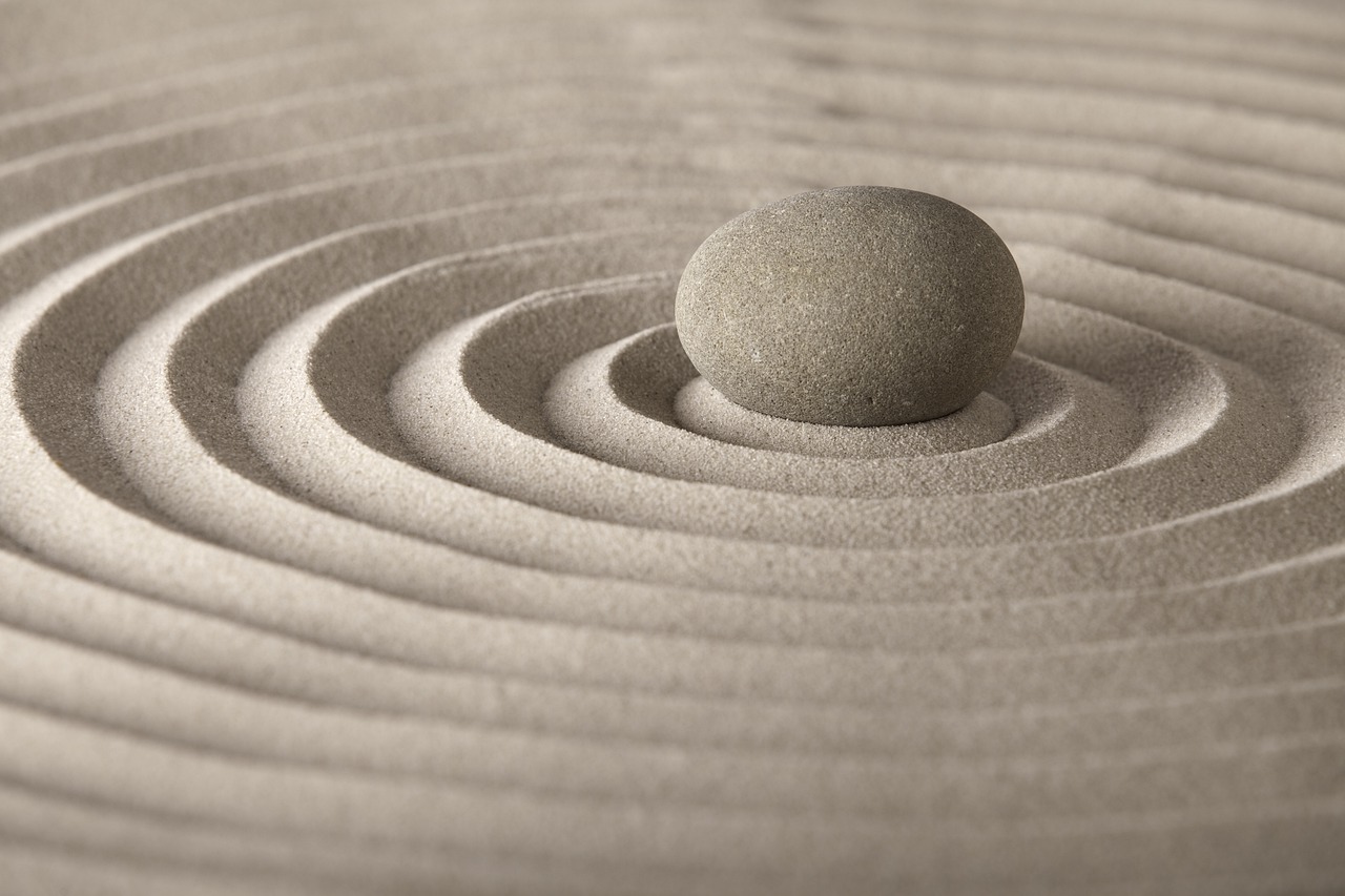 A stone sits in the center of sand with a pattern in it.