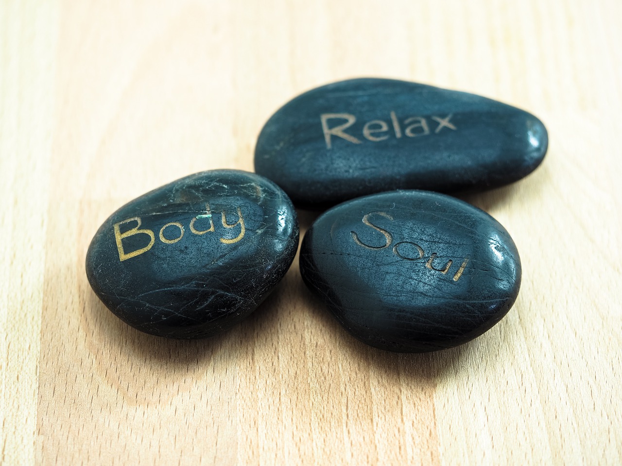 Three Vishuddha stones placed on a table with the words relax, soul, and body written on them.