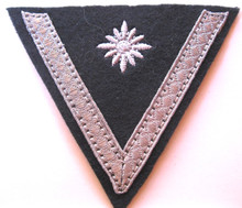 WW2 German Army Stabsgefreiter Sleeve Chevron, machine embroidered four pointed 'pip' and applique aluminum tress chevron on an inverted dark blue green wool triangle with backing.