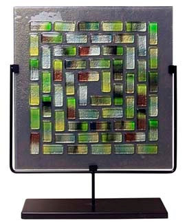A decorative fused glass square panel featuring a grey background with multicolored glass tiles in a pattern. Greens, yellows, blues and white