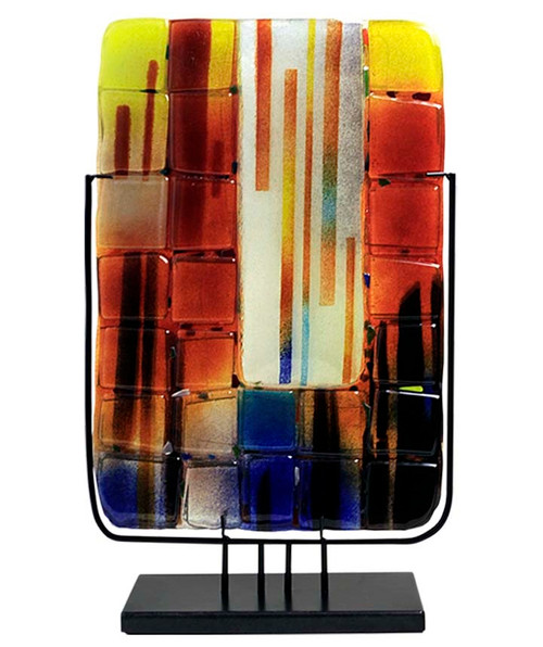A tall, rectangular vase with square glass appliques applied and fused in place.  Blue, black, red, orange and yellow.  Stand included