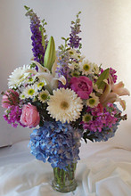 Trumpet vase filled with hydrangea, roses, gerberas, lilies, and larkspur.