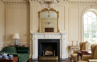 The crisp white Neoclassical mantel takes pride of place on a central breast wall, framing a deep black fireplace opening complete with traditional brass andirons.