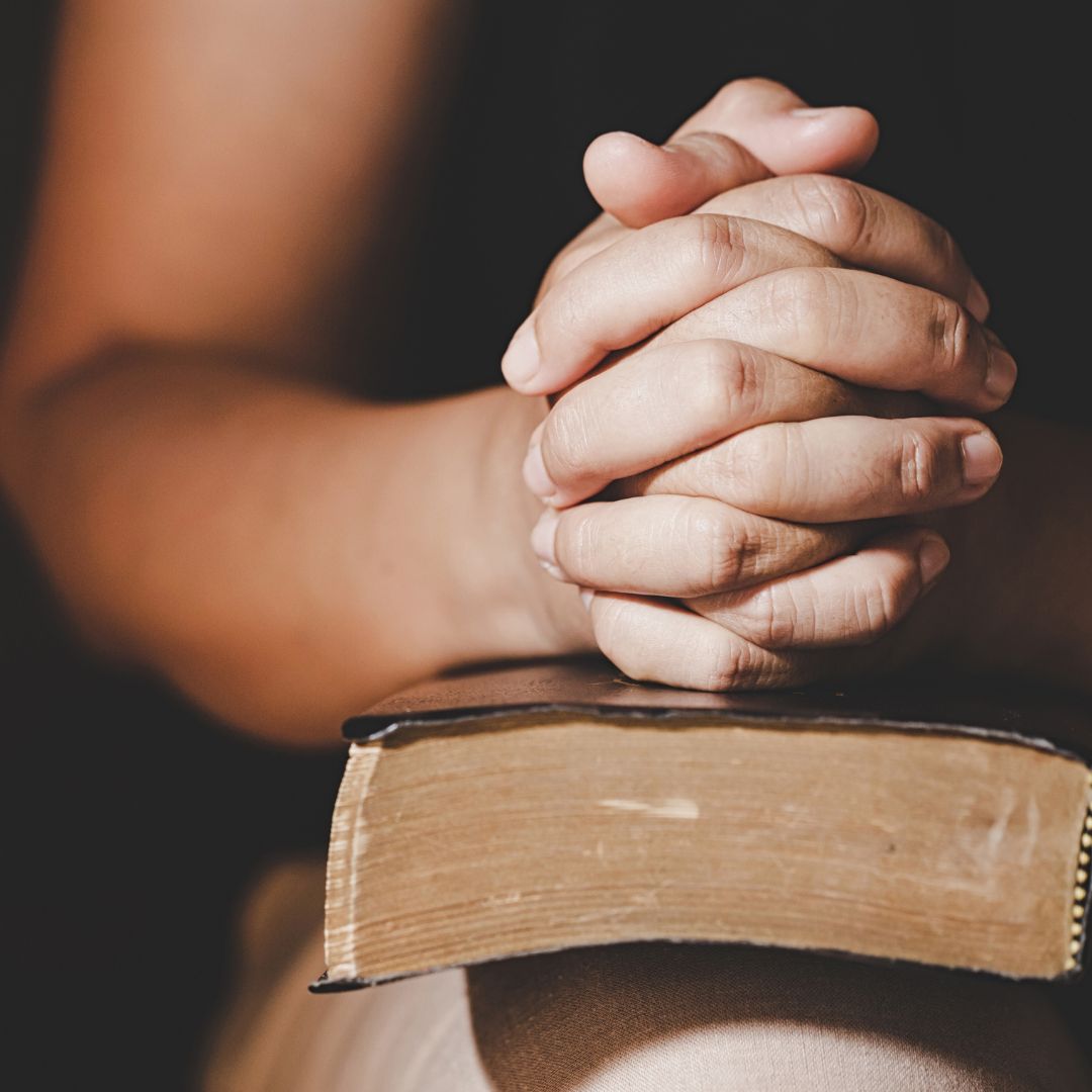 hands in prayer on top of thick book