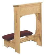 A red kneeling pad connected to a wooden, rectangular shelf with a cross on the side.
 