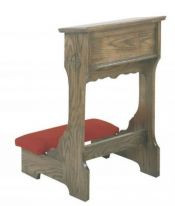 A red kneeling pad connected to a wooden, rectangular shelf with a cross on the side.