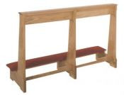 Rectangular wooden structure with a red kneeling pad and three legs holding up a shelf for prayer.