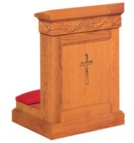 Rectangular wooden structure with a kneeling pad and decorative cross carved into the front.