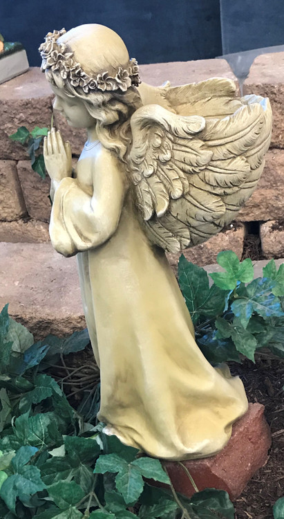 The side view of a praying angel standing on a rock in an outdoor garden.