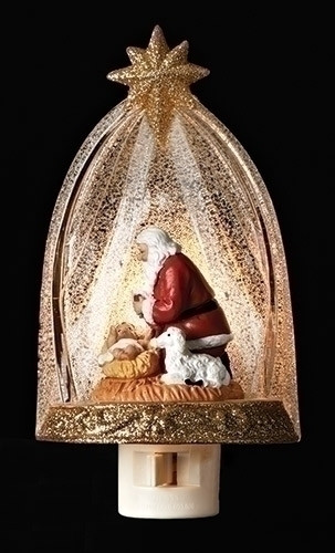 Night light with Santa kneeling next to baby Jesus in a crib and a glittery dome over them. 
