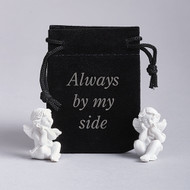 A cloth bag that says “Always by my side” propped next to two small white angel figurines. 1.25" Guardian Angel in a Pouch. Pouch says "Always by My Side" Please note: ONE ANGEL PER POUCH!