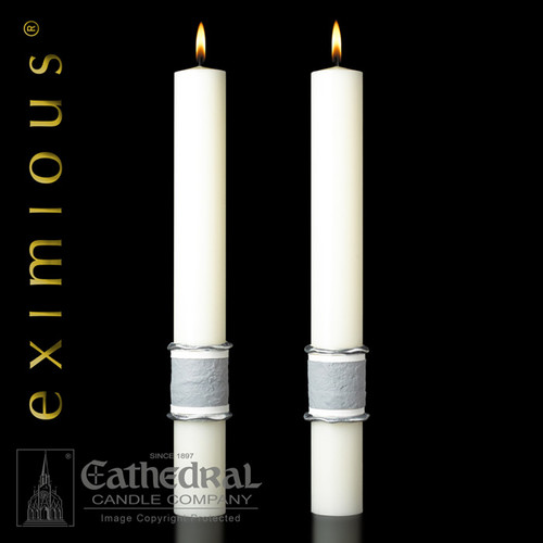Two white altar candles with silver/grey wrap around the bottom.
