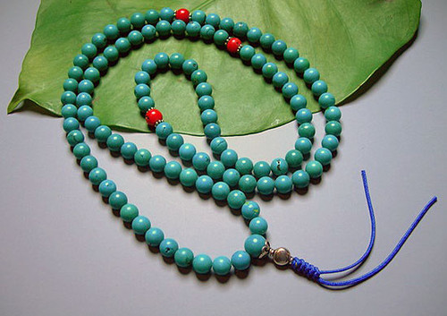 Turquoise 111 bead mala with three coral accents and knotted tassel. 